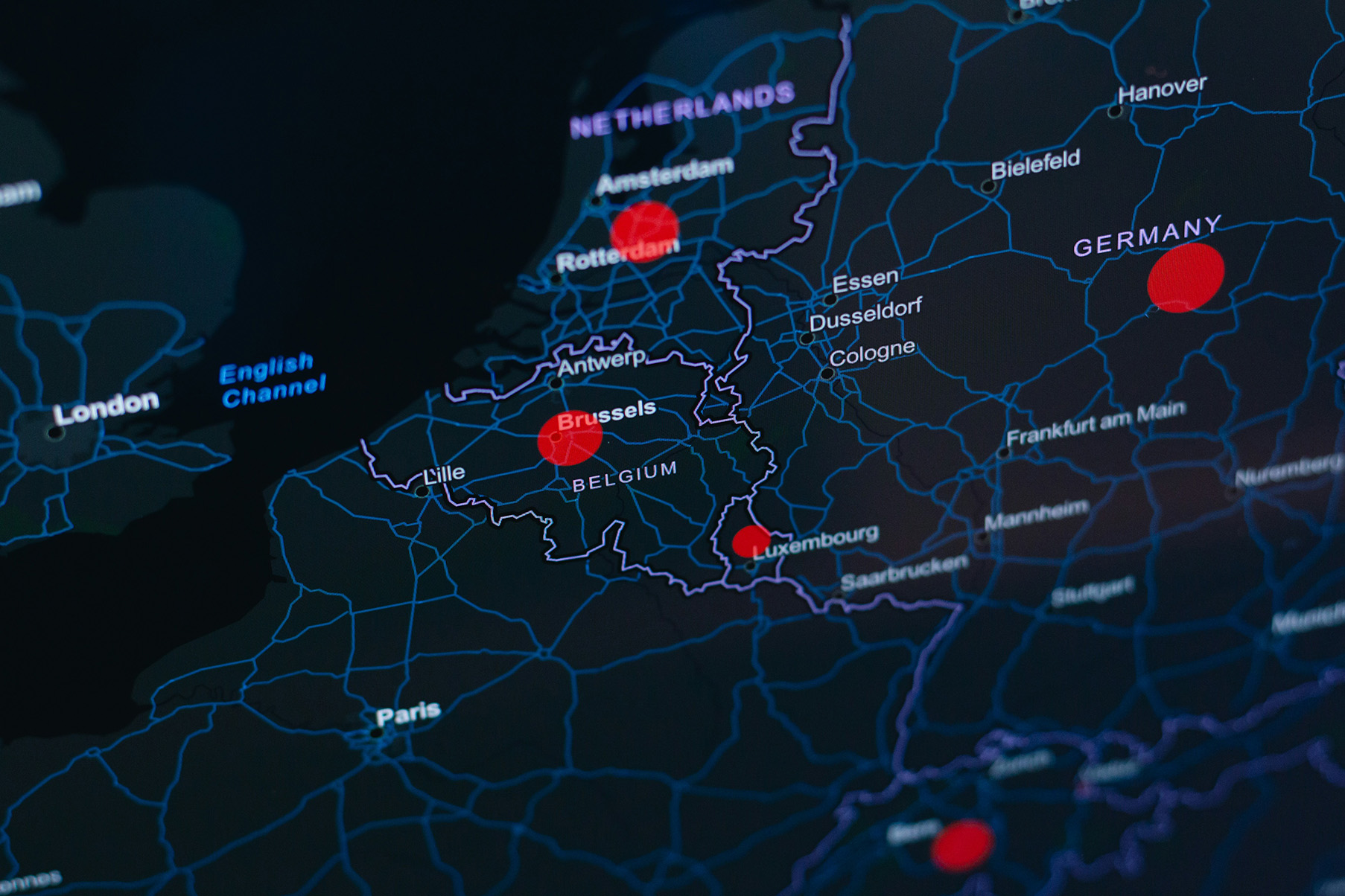 Dark digital map of Western Europe showing country borders and cities, with red location pins marking Rotterdam, Brussels, Luxembourg, and a point in Germany.